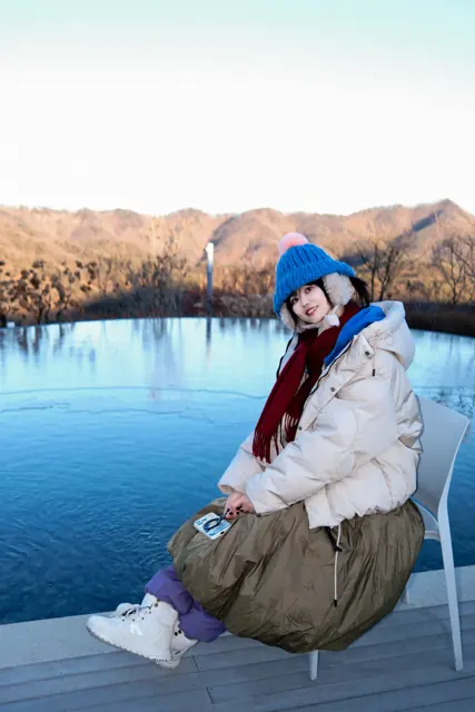 Kiwi in a blue hat beside a reflective pool in winter sunlight
